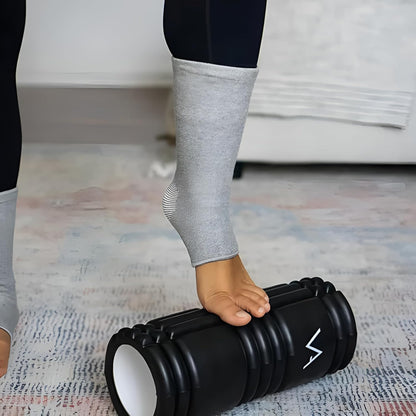 Foot massaging on black foam roller, person in grey compression socks, IndianChic wellness product