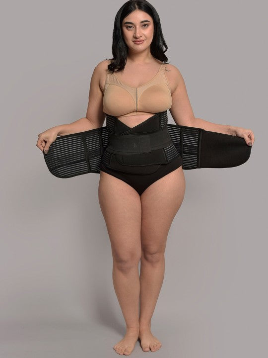 Woman wearing black 3-in-1 postnatal shapewear belt over underwear, hands spreading side straps