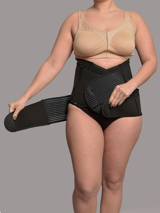 Woman wearing black 3-in-1 postnatal shapewear, adjusting abdominal support belt