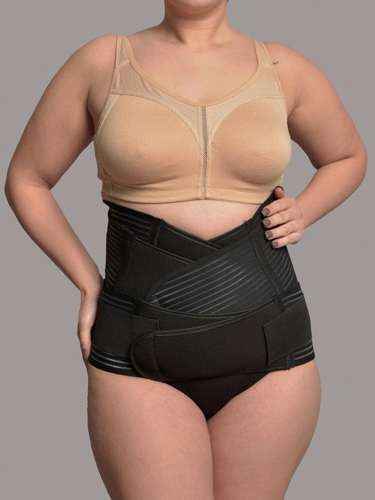 Woman wearing black 3-in-1 postnatal shapewear and nude support bra on gray background